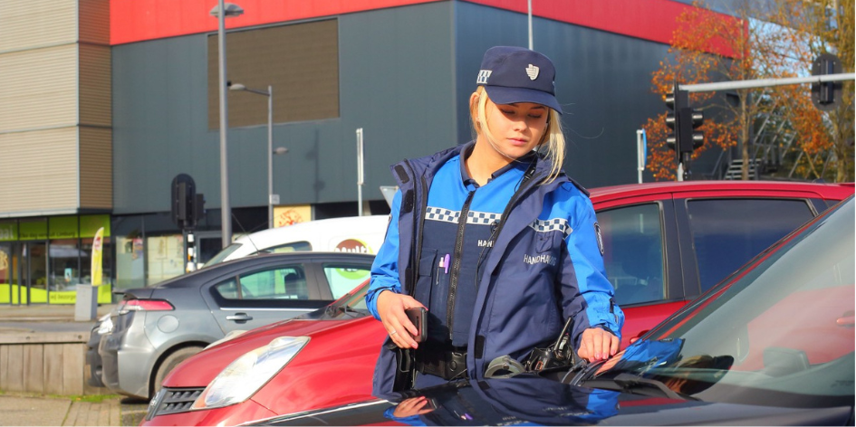Een vrouwelijke BOA in opleiding die voor de handhaving parkeercontroles houdt. 